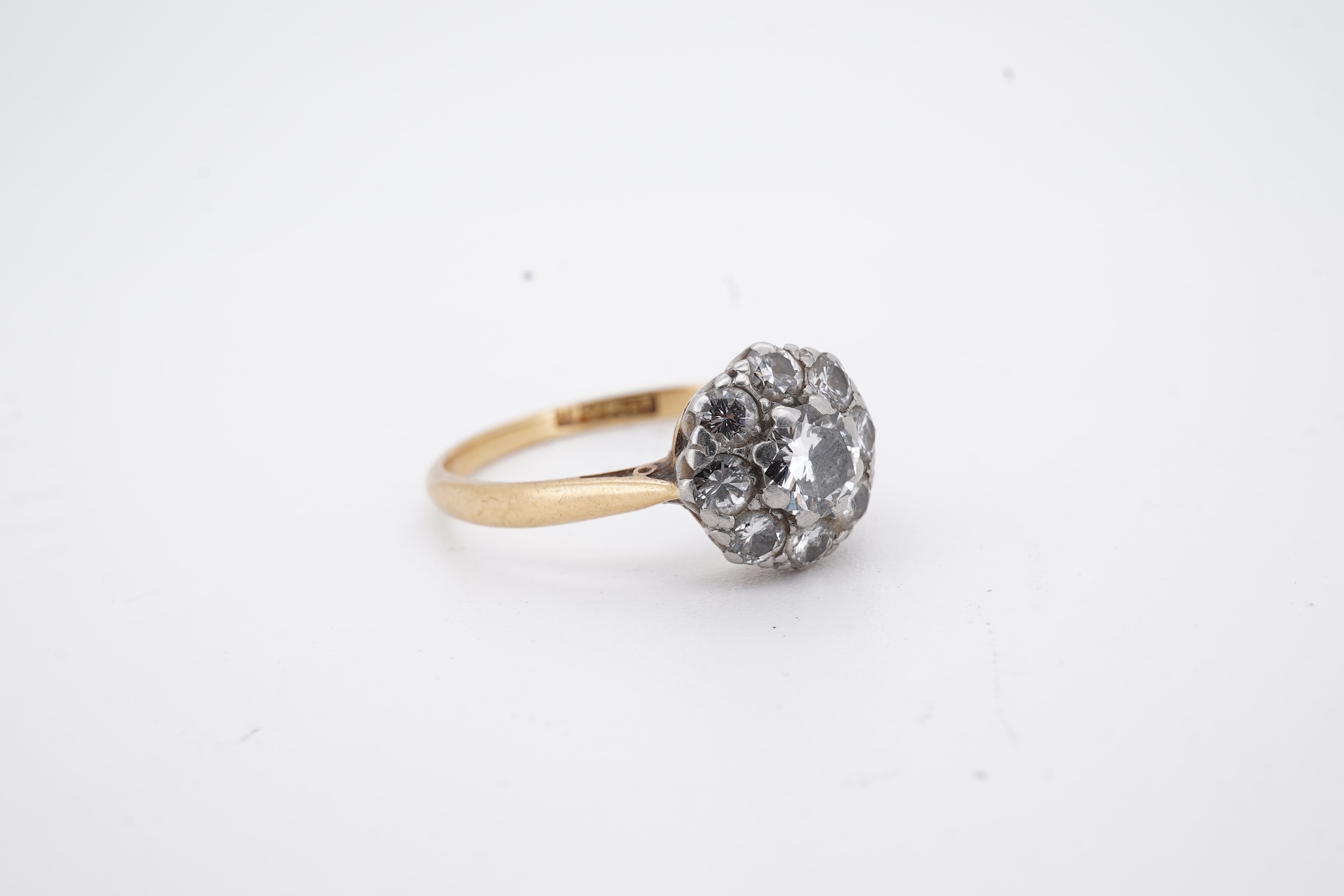 An early 20th century 18ct, plat. and nine stone diamond cluster ring, the central diamond weighing approximately 0.30ct, size Q, gross weight 3.1 grams.